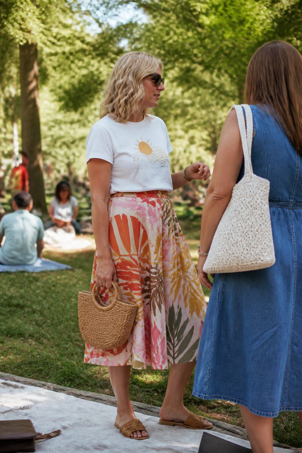 A woman stands in a park wearing a skirt and a graphic tee.