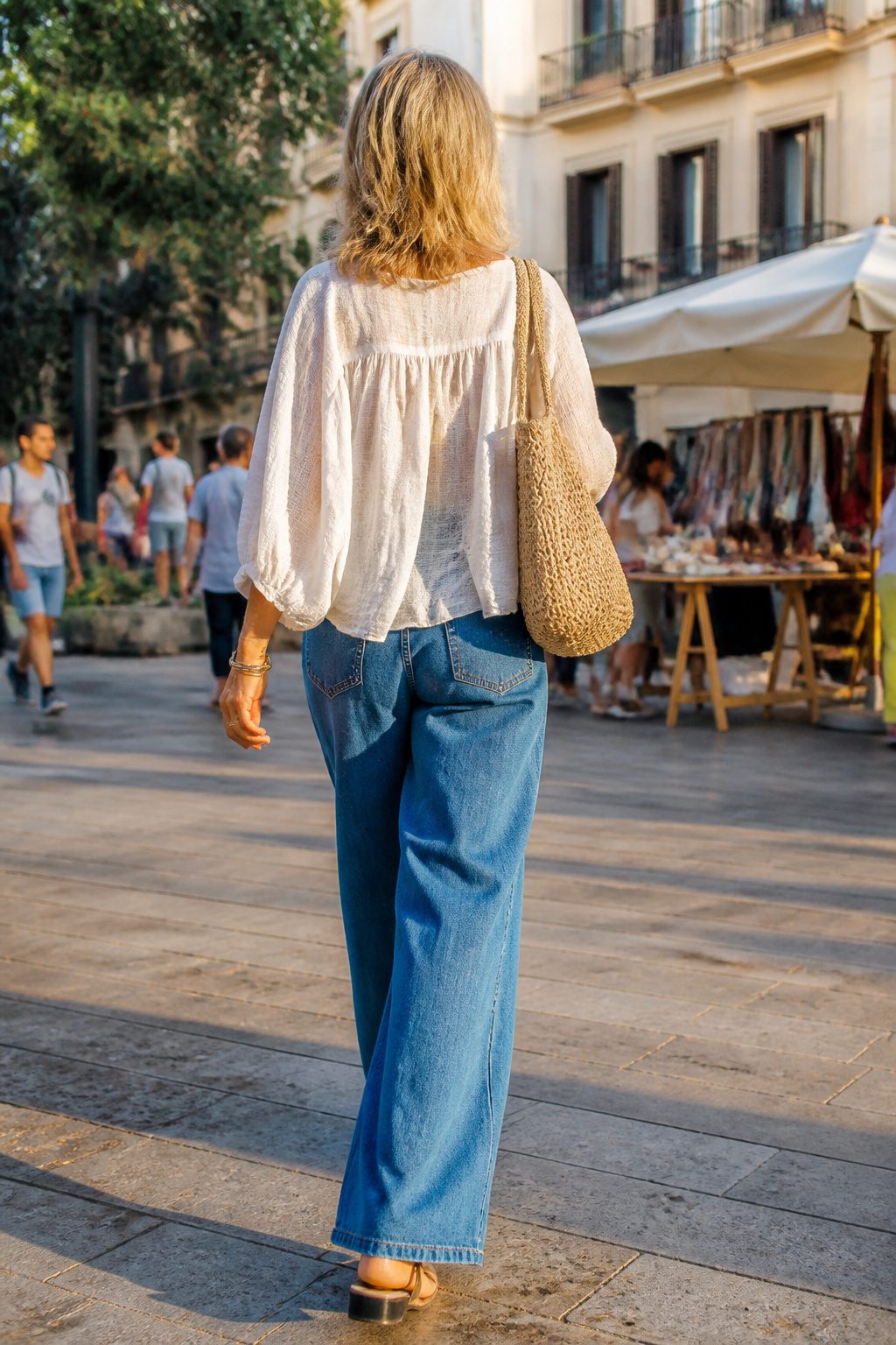 A woman strolls in wide-leg jeans and a gauze top in an urban area.