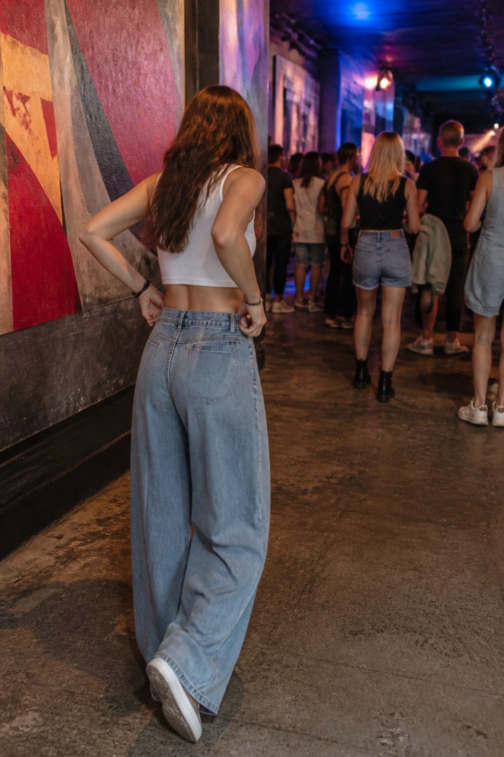 A model adjusting her wide-leg jeans as she enters a venue.