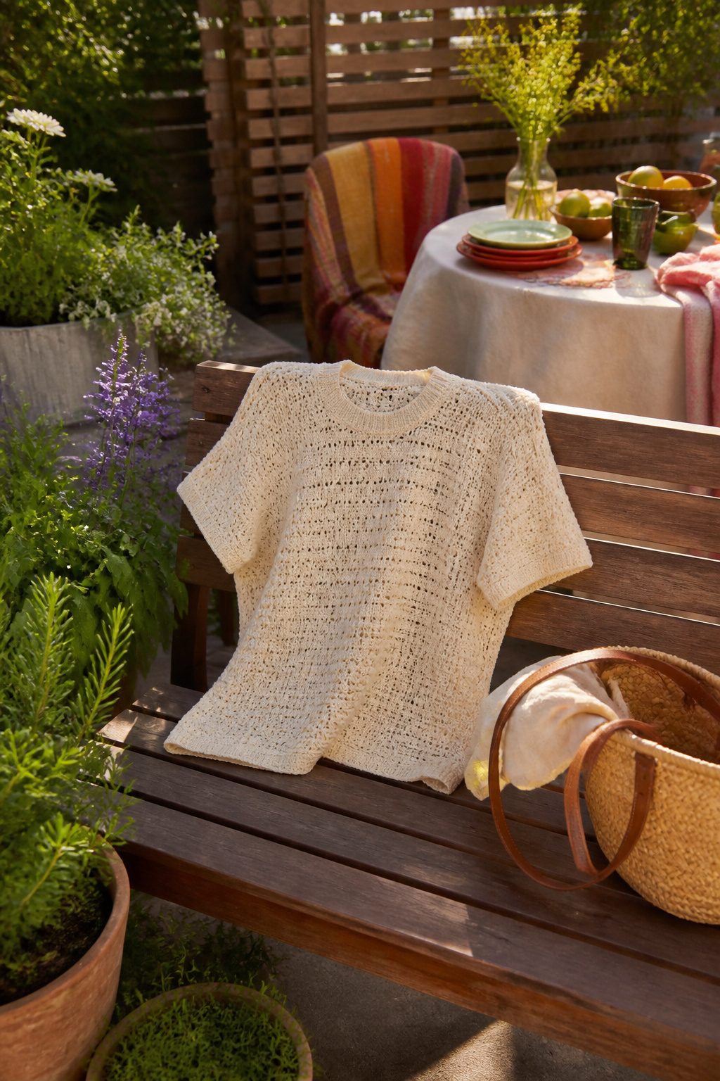 Crochet Summer Top Patterns, Styles and Yarn Guide 8 A Wren Tee displayed on a wooden bench with potted herbs.