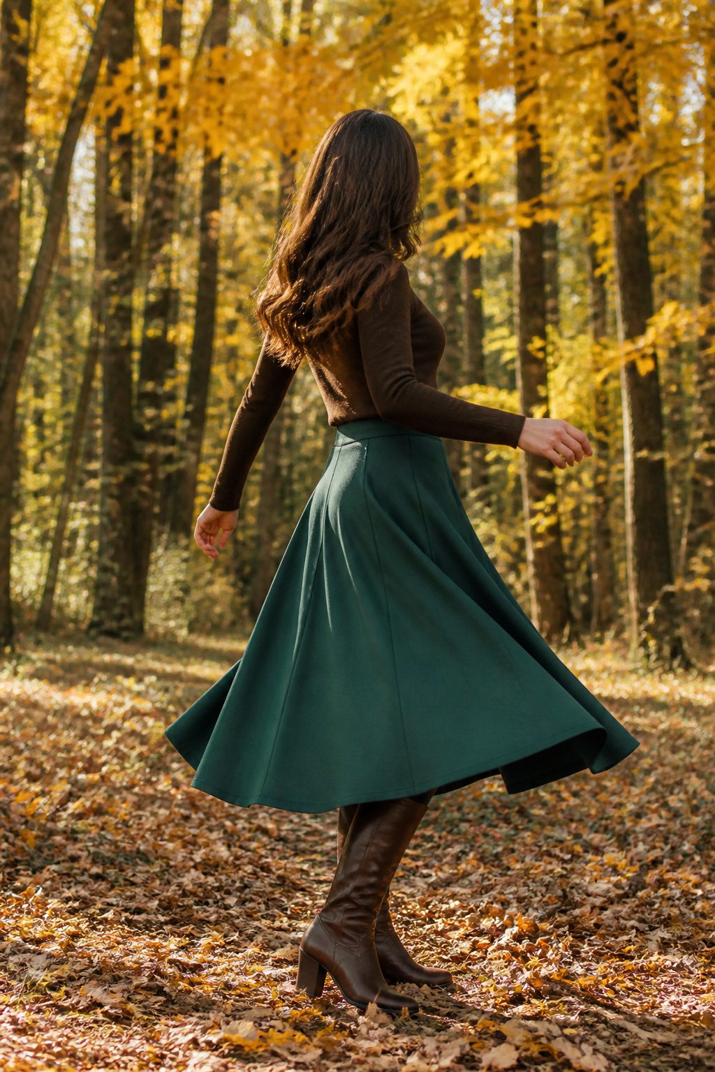 16 Fall Outfit Ideas to Build Your 2026 Wardrobe 8 Model in a green wool skirt surrounded by autumn leaves.
