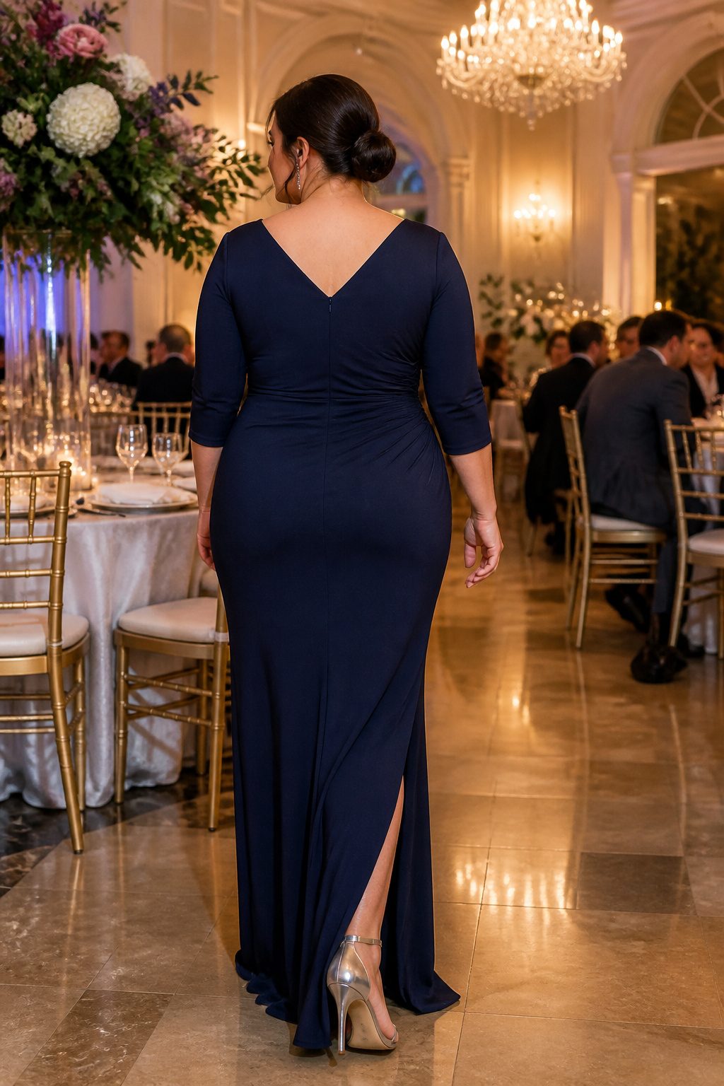 A model showcasing a plus size long cocktail dress in a banquet hall.
