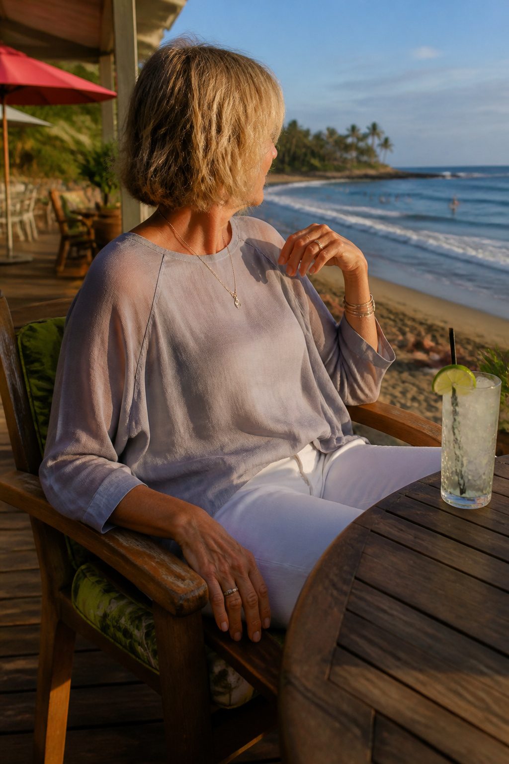 A woman seated at a café in a raglan sleeve top and white jeans.